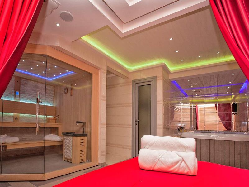 Moderner Spa-Raum mit Sauna, rotem Bett, weißen Handtüchern und indirekter LED-Beleuchtung.