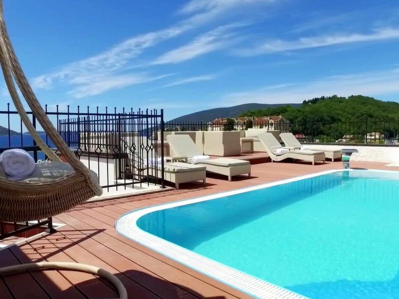 Dachterrasse mit klarem Pool, Liegestühlen, Hängebett und Panorama auf grüne Hügel und blauen Himmel.
