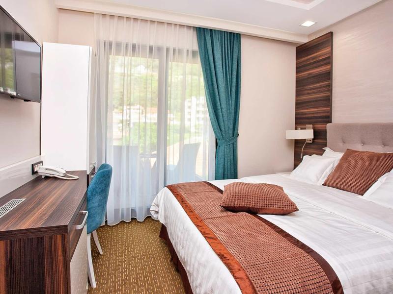 Gemütliches Schlafzimmer mit großem Bett, braunen Akzenten, Schreibtisch und blauem Vorhang.