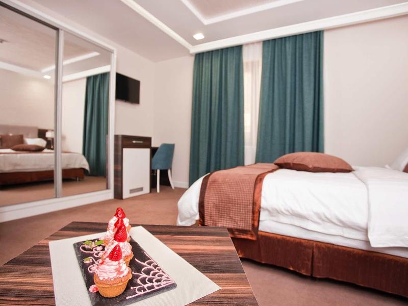 Schlafzimmer mit großem Bett, braunen Vorhängen, Spiegelschrank und kleiner Sitzecke.