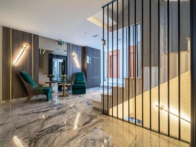 Moderner Raum mit Marmorfliesen, grünen Sesseln, vertikalen Metallstäben und indirekter Beleuchtung.