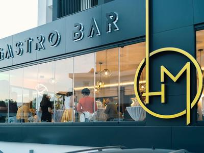 Moderne Gastro Bar mit großen Fenstern und Logo in goldener Farbe an der Fassade.