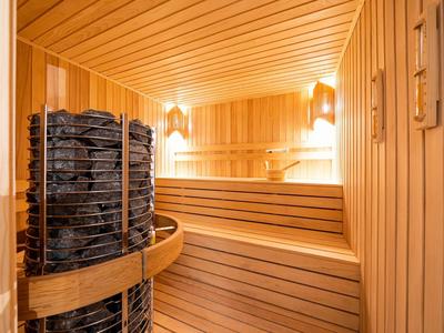 Helle Sauna mit Holzverkleidung, steinbeheiztem Ofen und mehrstufiger Sitzbank.