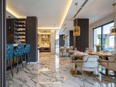 Eleganter Essbereich mit weiß-grau gemusterter Marmorboden, blauen Barhockern und goldenen Lampen.