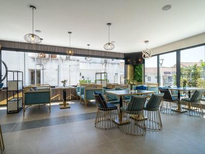 Moderner, heller Gastraum mit grauen Stühlen, runden Tischen und großen Fenstern zur Straßenseite.