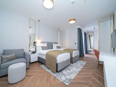 Helles, modernes Schlafzimmer mit Doppelbett, Teppich, Sofa, Fernseher und Schreibtisch in neutralen Farben.