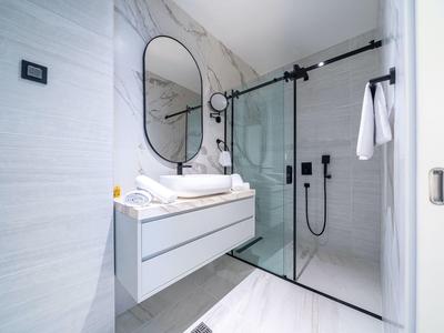 Helles Badezimmer mit runder Spiegelfläche, hängendem Waschbecken und Glas-Duschabtrennung.