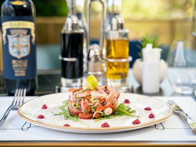 Auf einem weißen Teller liegt ein kunstvoll angerichteter Salat mit Lachs, garniert mit Kräutern und Granatapfelkernen.