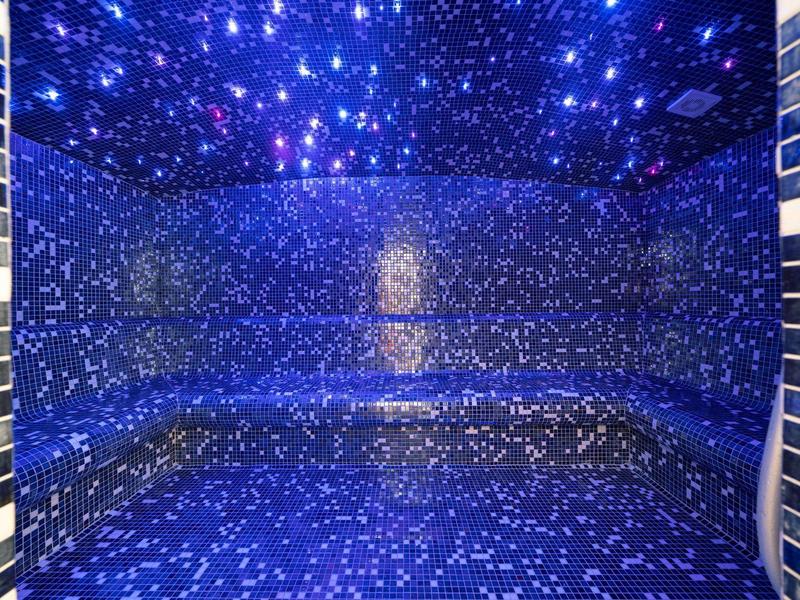 Blau beleuchteter Raum mit glitzernden Sternenmustern an Wänden und Decke, ovaler Sitzfläche.