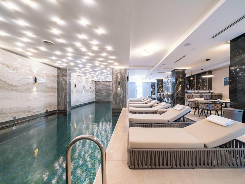 Moderner Wellnessbereich mit Innenpool, Liegen und stilvoller Beleuchtung an weißer Decke.