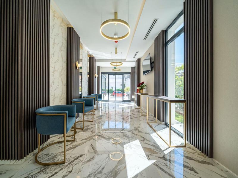 Moderner Flur mit weißem Marmorboden, blauen Sesseln und goldfarbenen Akzenten, helle Beleuchtung.