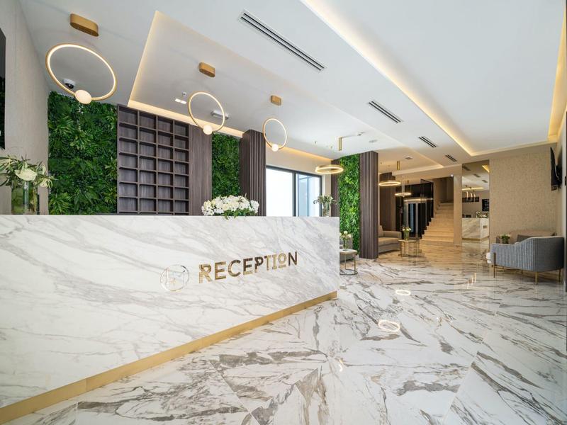 Helle Empfangshalle mit Marmortheke, grünem Wanddekor und moderner Beleuchtung.