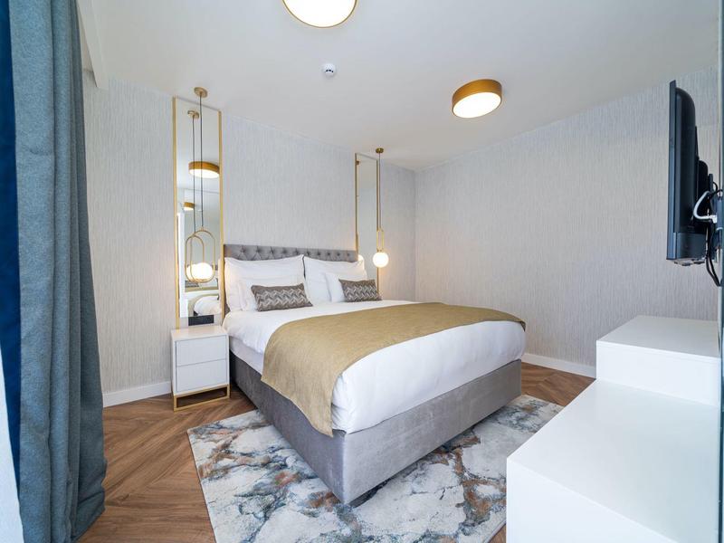 Modernes Schlafzimmer mit Doppelbett, Teppich, Nachttischen, Hängelampen und Wandfernseher.