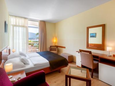 Helles Hotelzimmer mit Doppelbett, Schreibtisch, Stuhl und Blick aus dem Fenster.