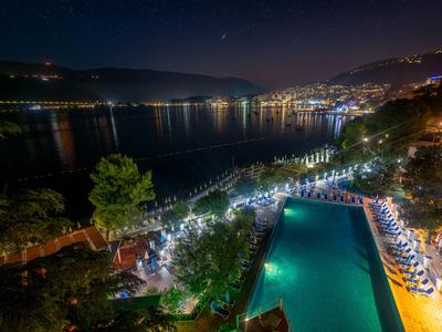 Nächtliche Aussicht auf einen beleuchteten Pool und Stadtlichter an einem Seeufer.