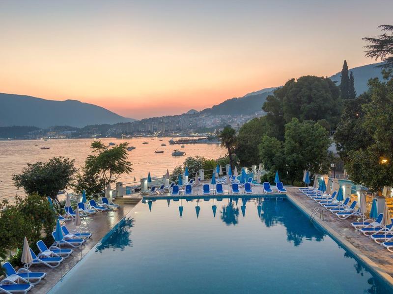 Poolbereich mit Liegestühlen und Blick auf See und Berge bei Sonnenuntergang