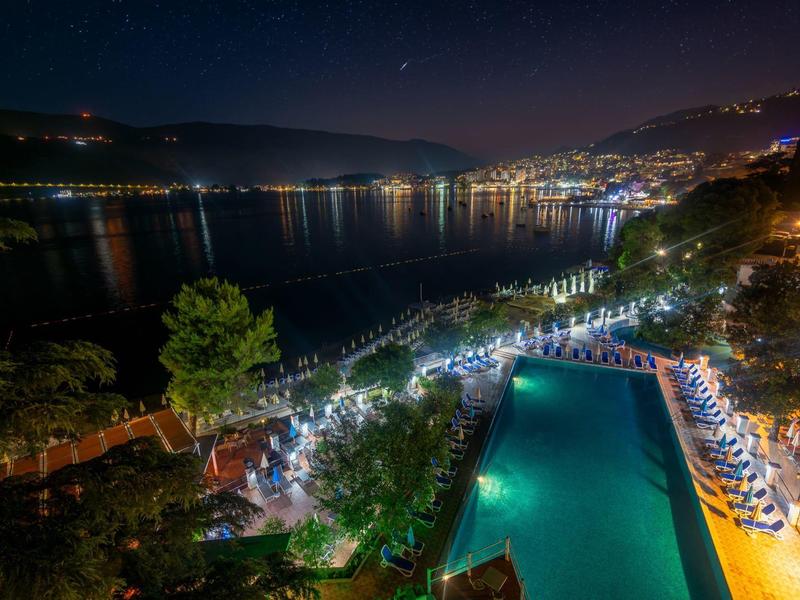 Nächtliche Aussicht auf einen beleuchteten Hotelpool und eine Stadt am Wasser