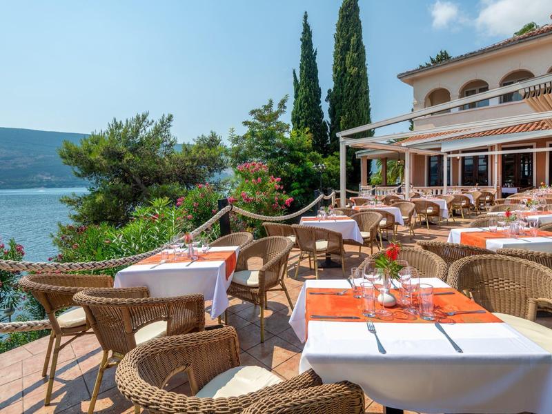 Terrasse eines Restaurants mit gedeckten Tischen und Blick auf das Meer und umliegende Berge.