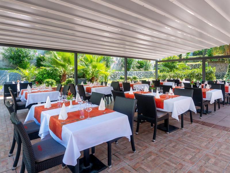 Überdachter Außenbereich eines Restaurants mit gedeckten Tischen und Blick ins Grüne.