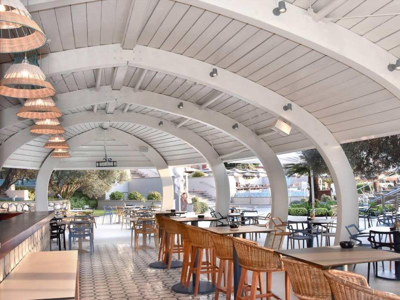 Moderner, heller Gastronomiebereich mit Holztischen, Stühlen und großen Gewölbedecken aus Holz.