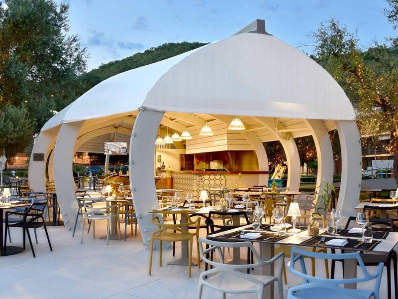 Moderner Außenbereich mit rundem, weißem Pavillon und vielen Holzstühlen bei Tageslicht.