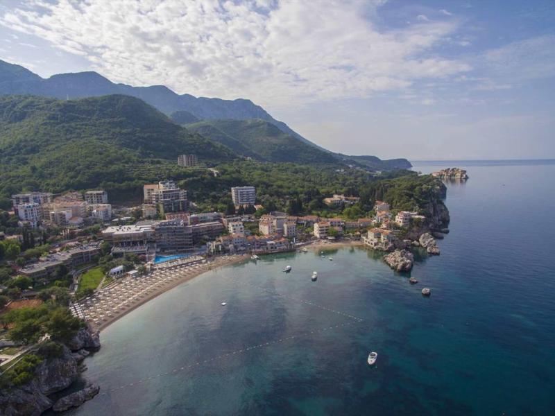 Kleine Küstenstadt mit Sandstrand, umgeben von grünen Bergen und klarem blauen Meer.