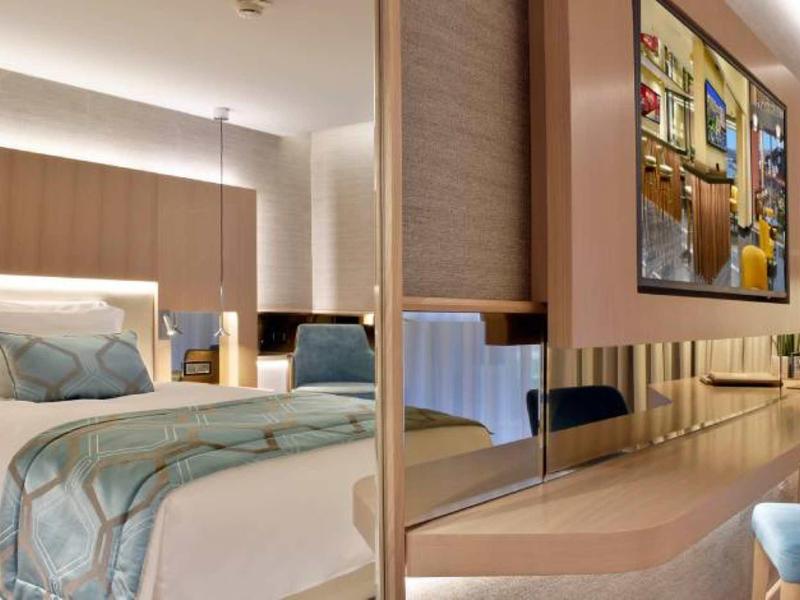 Modernes Hotelzimmer mit großem Bett, weicher Bettdecke, Holzverkleidung und Fernseher an der Wand.