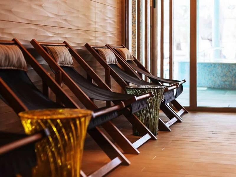Holzliegen mit schwarzen Stoffbezügen neben einer Glaswand in warm beleuchtetem Raum.