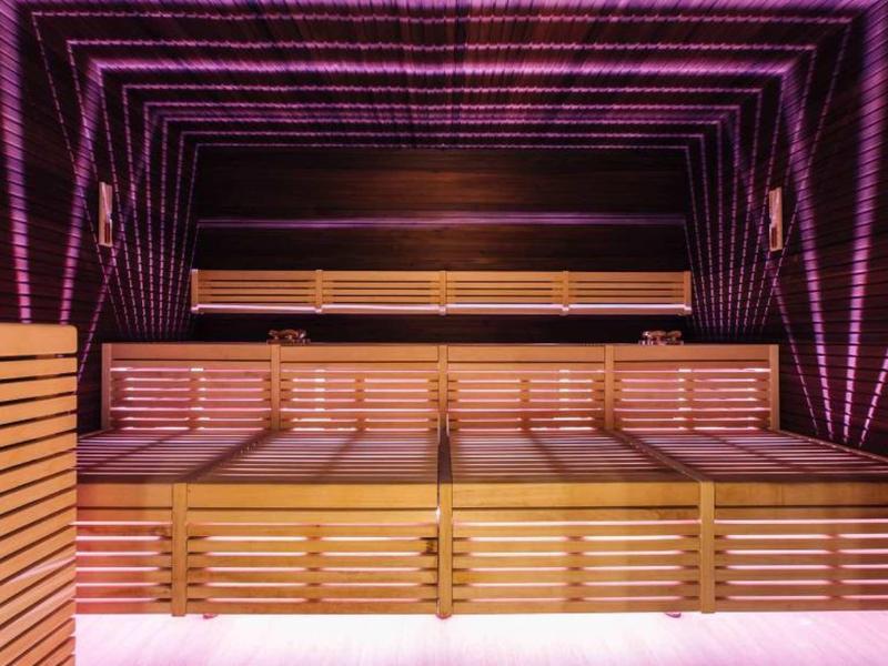 Moderne Sauna mit Holzliegen, lila LED-Beleuchtung und spiegelnden Wänden.