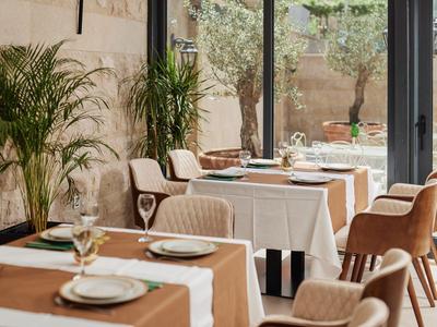 Restaurante elegante con mesas puestas y sillas frente a grandes ventanas con vista al patio.