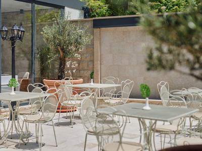 Leerer Außenbereich mit weißen Metallstühlen und Tischen, grüne Pflanzen als Dekoration.