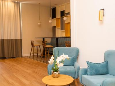 Moderner Wohnraum mit hellblauem Sessel, kleinem runden Holztisch und offener Küche im Hintergrund.