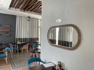 Moderner Gastraum mit blauen Stühlen, Teppichboden, Holzdeckenbalken und ovalem Wandspiegel.