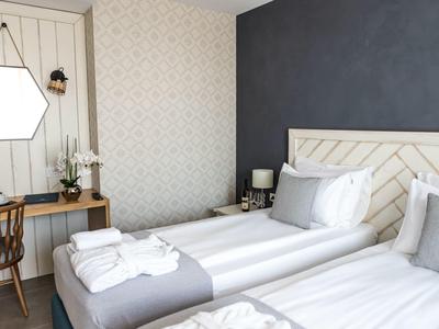 Hell eingerichtetes Schlafzimmer mit zwei Einzelbetten, Holzstuhl, Wandspiegel und Dekoration.