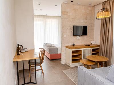 Kleines, modernes Hotelzimmer mit Schreibtisch, Bett, Sofa, TV und Fenster mit Vorhängen.