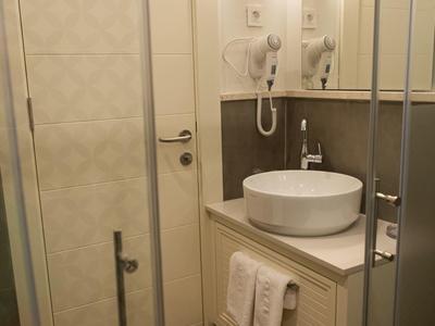 Kleines Badezimmer mit weißer Keramik-Waschschüssel, Handtüchern und Föhn an cremefarbener Wand.