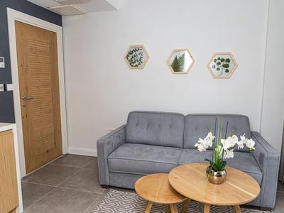 Kleines Wohnzimmer mit grauem Sofa, zwei runden Holztischen und dekorativen Wandspiegeln.