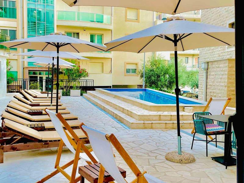 Sonnenschirme und Liegestühle stehen um einen kleinen Pool in einem Innenhof mit gelben Gebäuden.