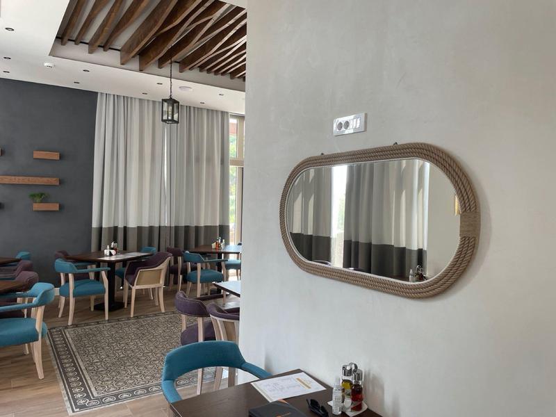 Moderner Gastraum mit blauen Stühlen, Teppichboden, Holzdeckenbalken und ovalem Wandspiegel.