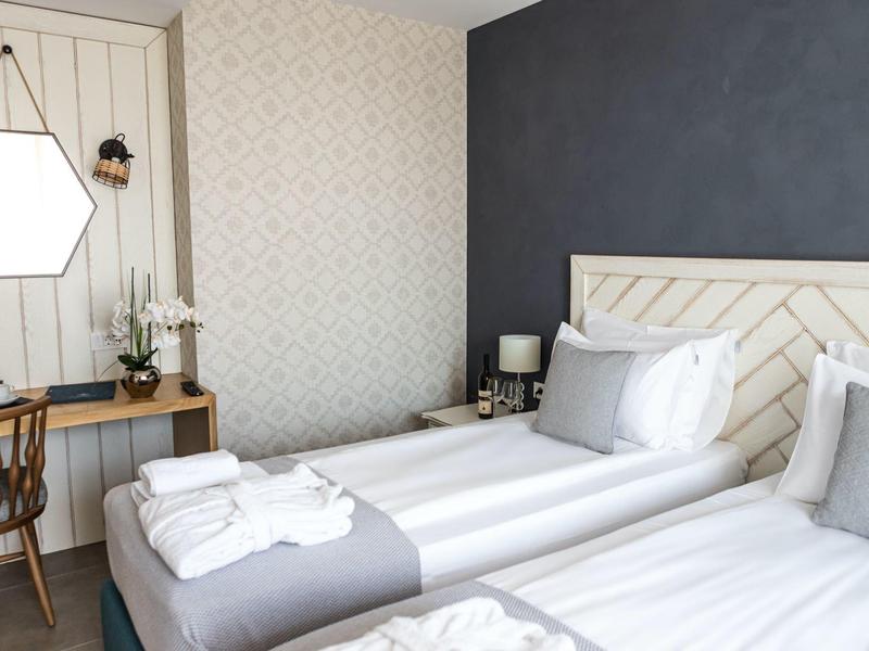 Hell eingerichtetes Schlafzimmer mit zwei Einzelbetten, Holzstuhl, Wandspiegel und Dekoration.