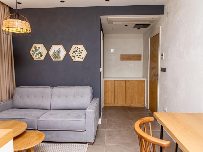 Gemütliches Wohnzimmer mit grauem Sofa, dunkler Wand, hölzernen Tischen, Stuhl und Wanddekoration.