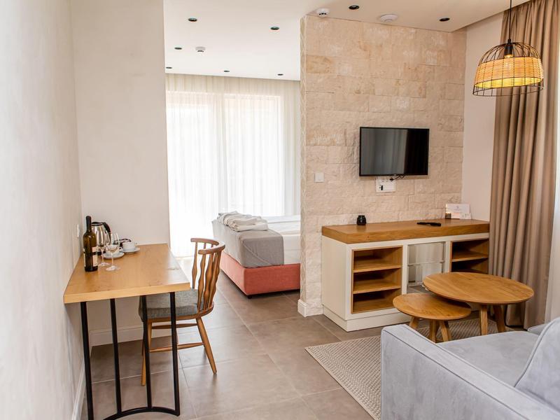 Kleines, modernes Hotelzimmer mit Schreibtisch, Bett, Sofa, TV und Fenster mit Vorhängen.