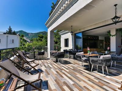 Große Terrasse mit Holzfliesen, Liegestühlen, Esstisch und Blick auf grüne Hügel bei klarem Himmel.