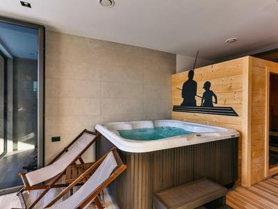 Moderner Wellnessbereich mit Whirlpool, Saunahaus aus Holz und zwei Liegestühlen aus Holz und Stoff.