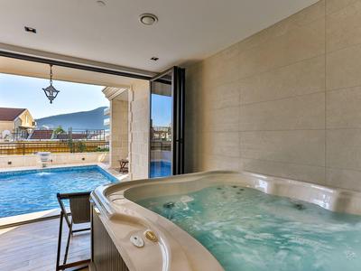 Innen-Jacuzzi neben großen Fenstern mit Blick auf Außenpool und Berglandschaft bei Sonnenschein.