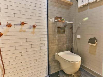 Modernes Badezimmer mit wandhängendem WC, grauen Fliesen und weiß gefliestem Duschbereich.