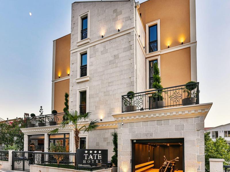 Modernes vierstöckiges Gebäude mit weißen und orangefarbenen Wänden, beleuchteten Fassaden und Balkon.