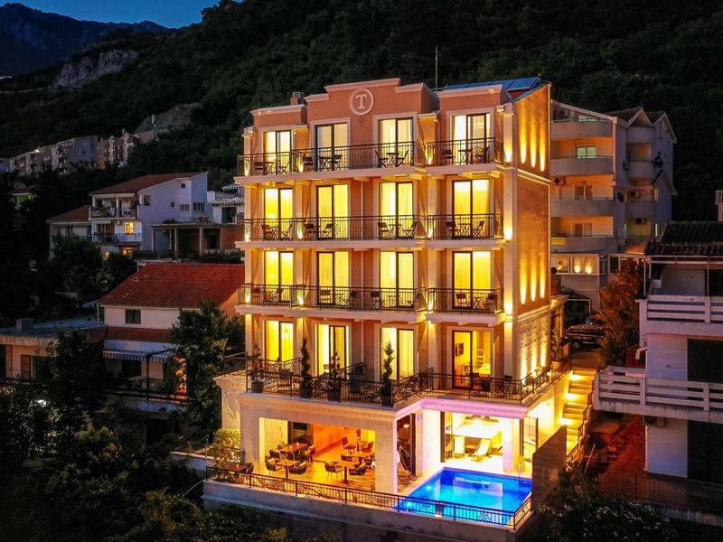 Modernes, beleuchtetes Haus mit Pool in bergiger, bewaldeter Umgebung bei Nacht.