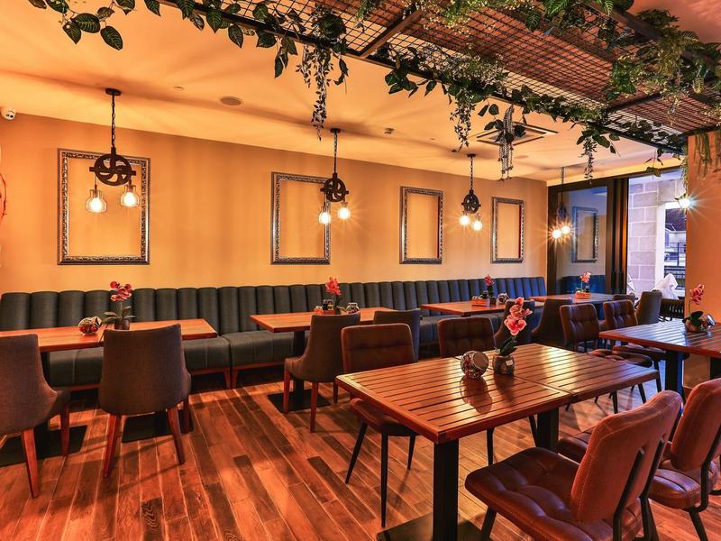 Gemütliches Restaurant mit Holztischen, grünen Sitzbänken, Lederstühlen und Pflanzen an der Decke.