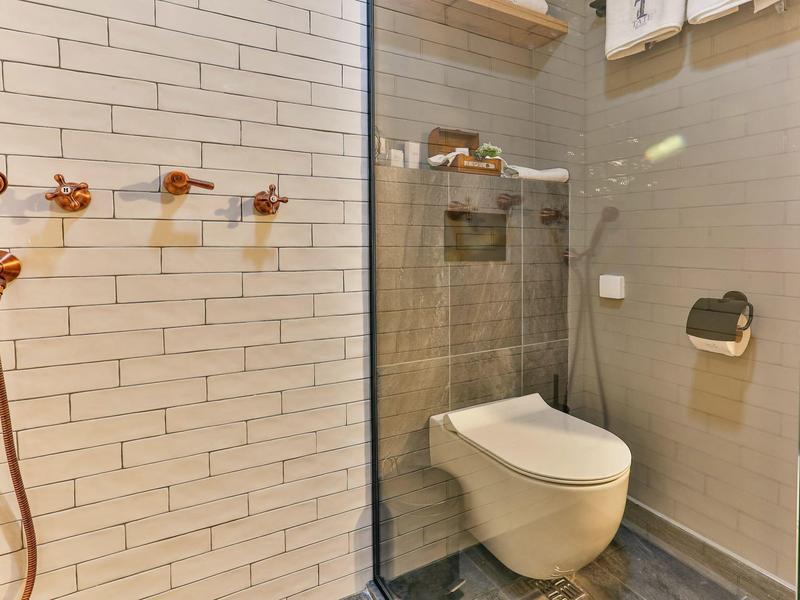 Modernes Badezimmer mit wandhängendem WC, grauen Fliesen und weiß gefliestem Duschbereich.